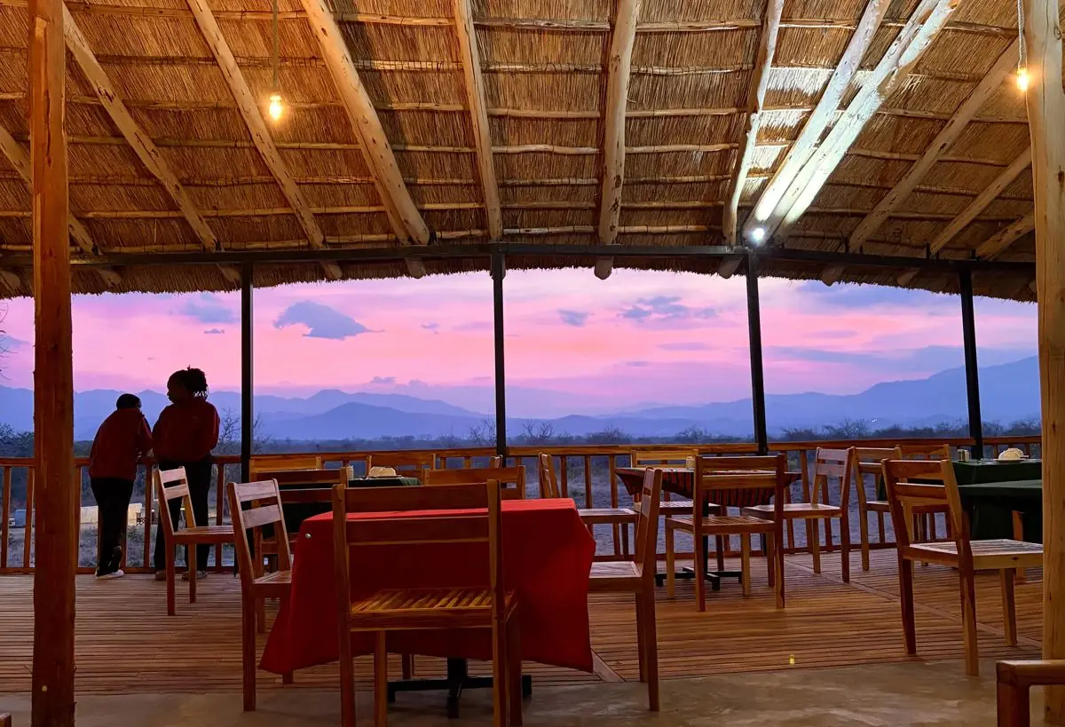 The Camp Lilac restaurant at dusk, open to the Mikumi mountain ridge under a pink sky